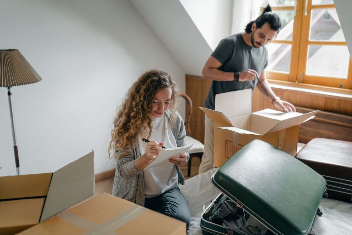 Un couple prépare ses cartons et ses valises dans une chambre lumineuse avant d'envoyer un modèle de lettre de demande de jour de congé déménagement.