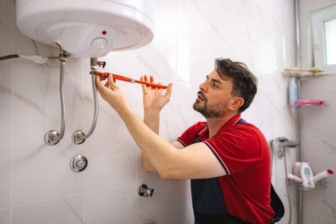 Un technicien en train d'installer un chauffe-eau électrique mural dans une salle de bain moderne.
