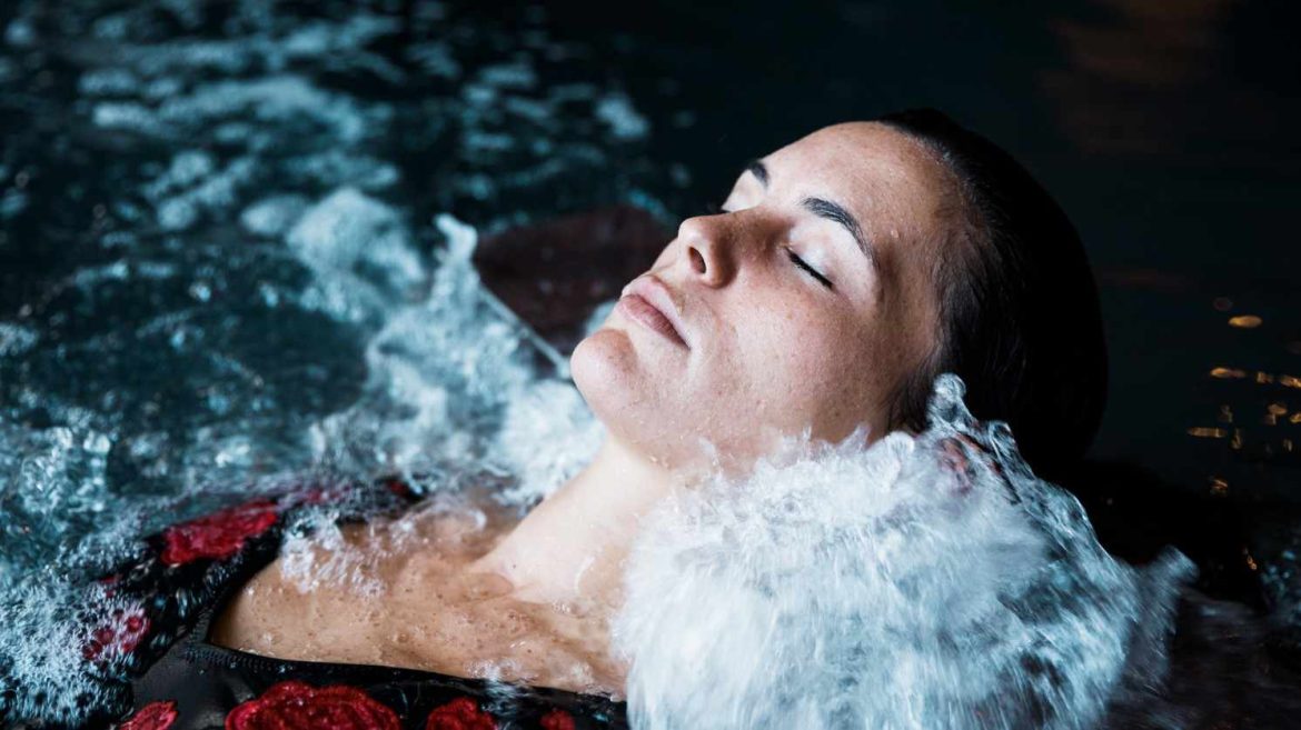 Une femme les yeux fermés se détend dans l'eau bouillonnante lors d'une séance de massage sous affusion eau et relaxation.